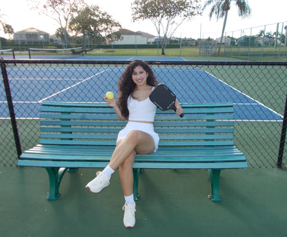 Woman sitting on tennis bench holding a NXTPick carbon fiber pickleball paddle and ball on court